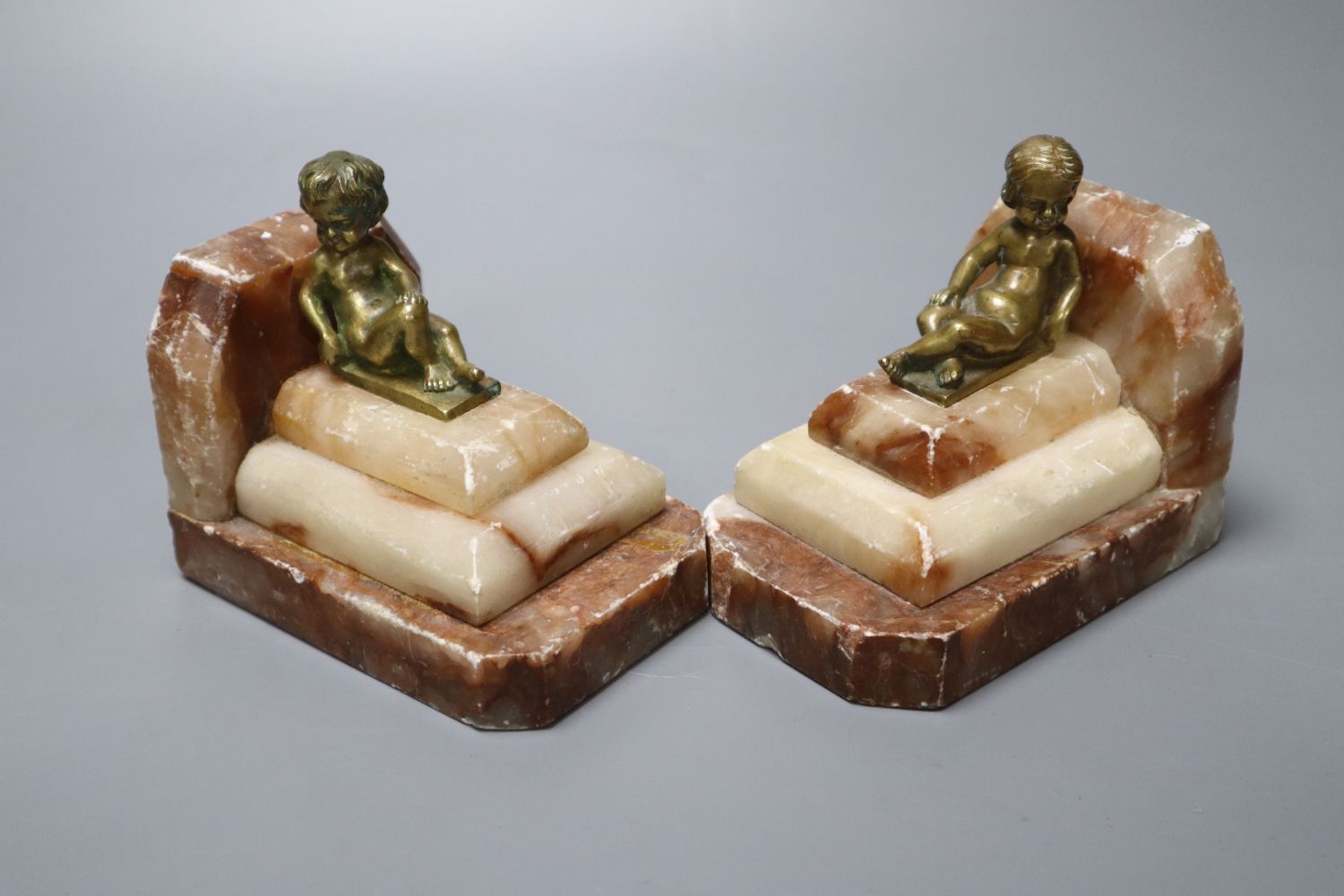 A pair of 1930s stepped marble book-ends, with seated youth surmounts, height 10cm